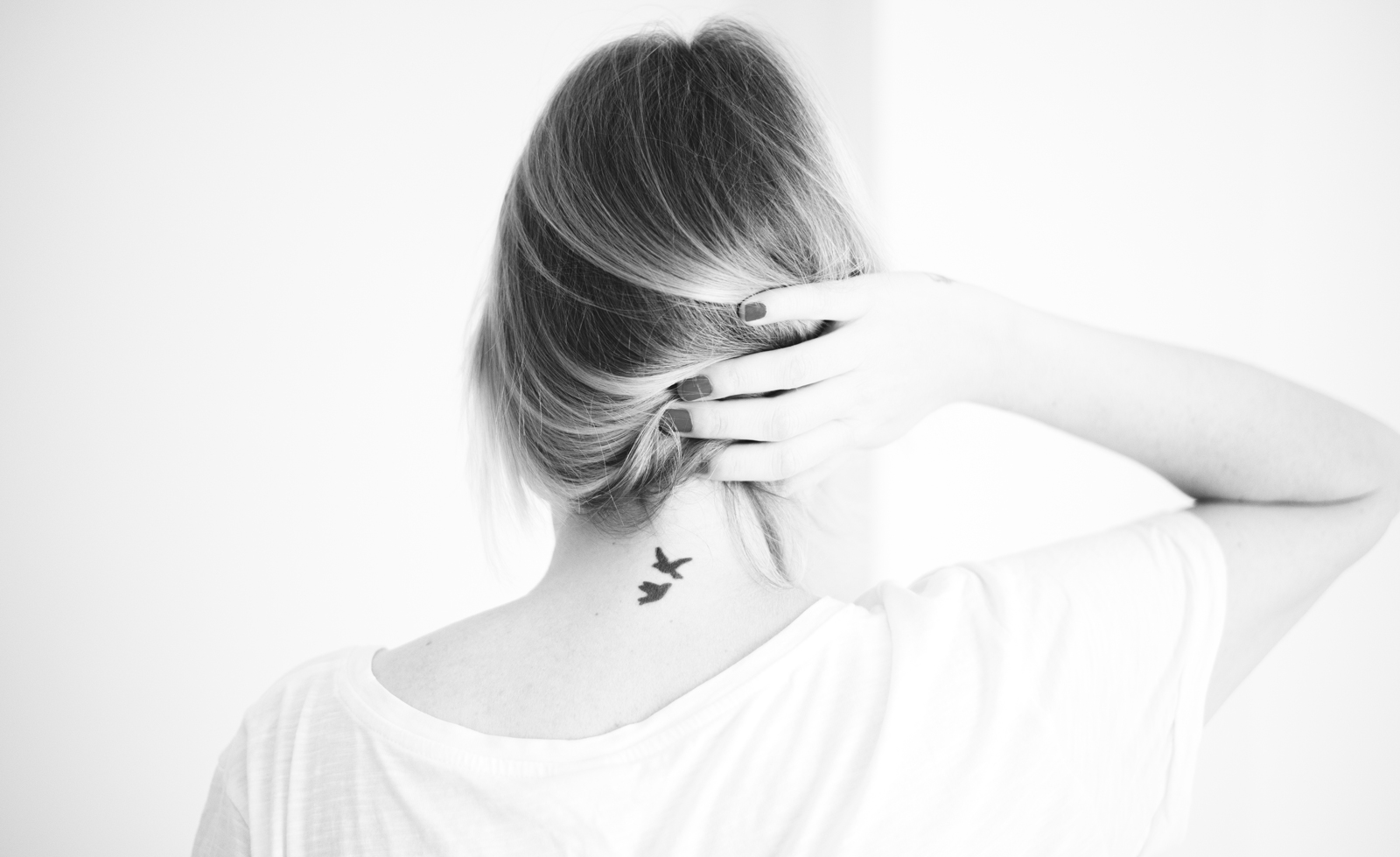 mujer por detrás, se está recogiendo el pelo para mostrar el tatuaje de dos pájaros que lleva en la nuca